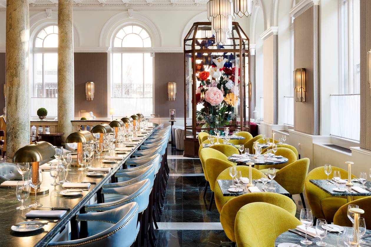 A large, opulent dining area at Riggs DC with grand columns and plush seating, featuring a large bouquet of flowers.