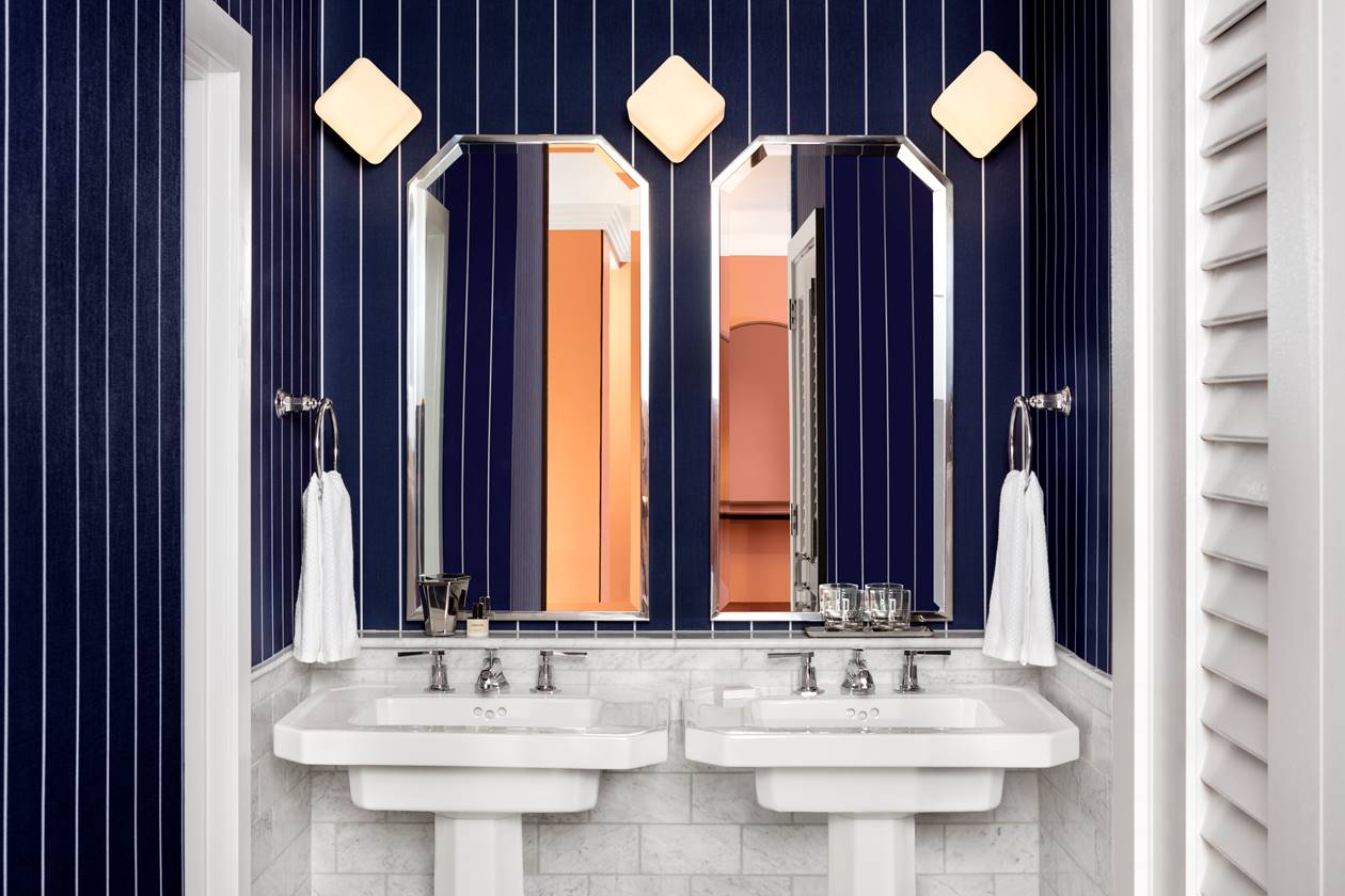 A bathroom with deep blue striped walls, twin pedestal sinks, and octagonal mirrors reflecting a warm-toned interior.