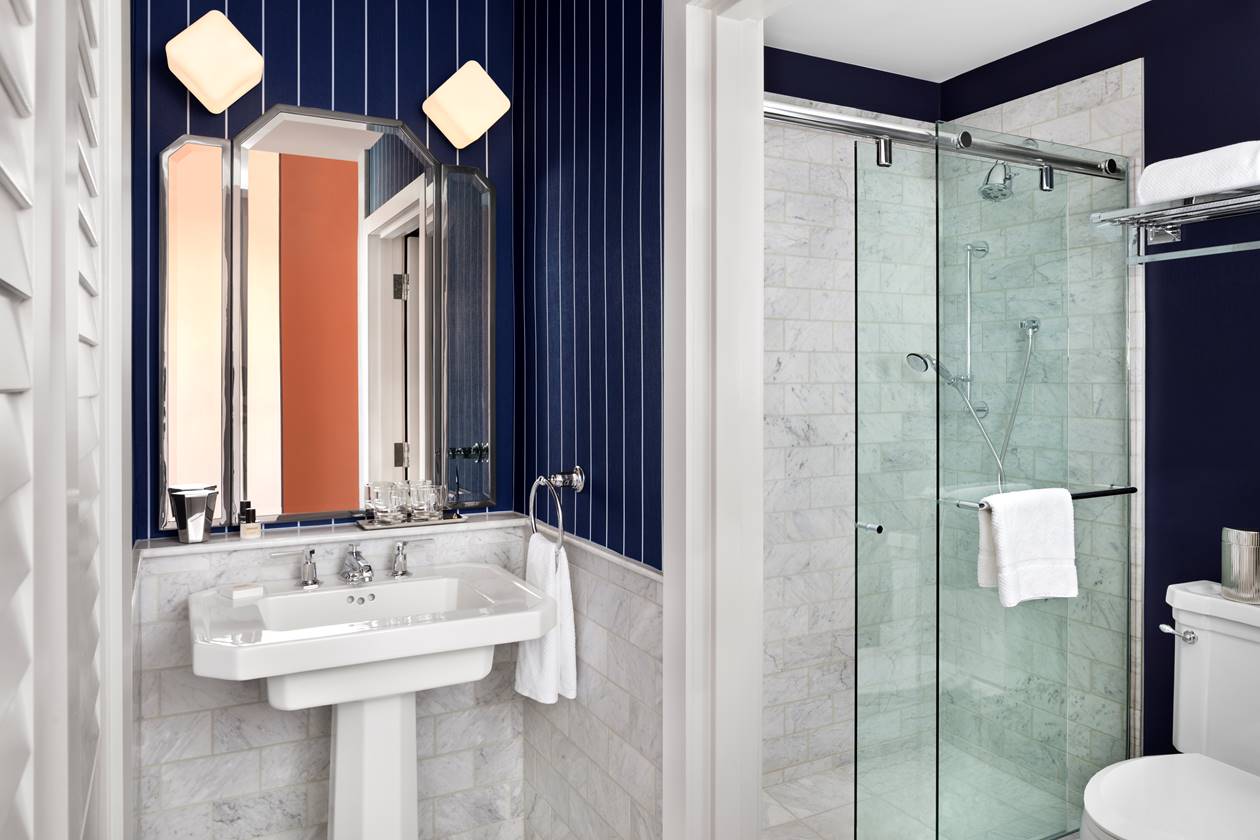 The bathroom of a deluxe room, showcasing modern chrome fixtures, sleek marble tiling and a spacious layout.